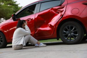 A woman sitting next to her car after a truck accident, wondering who is liable.