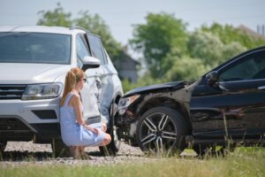 A woman sitting next to her crashed car, wondering about the five things to do after a car accident in Virginia.